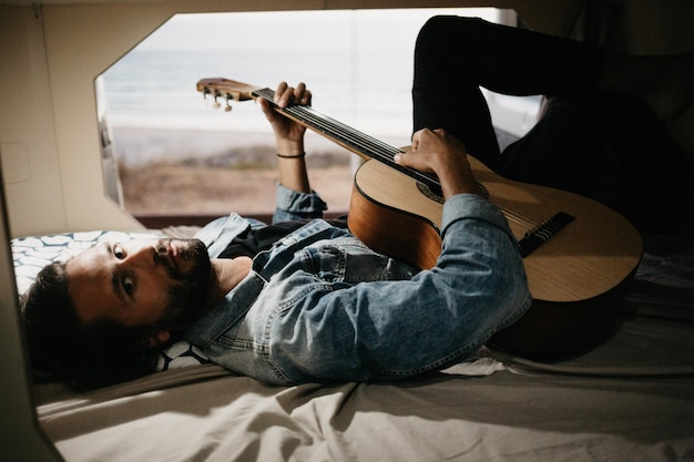 Photo man playing guitar while lying down on bed