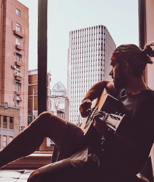 Photo man playing guitar while sitting on window sill