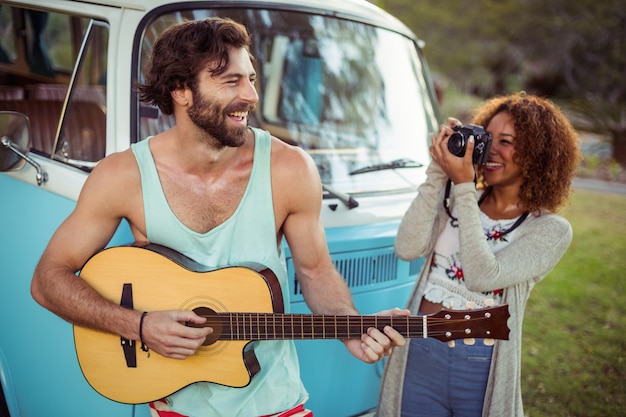 Man playing guitar while woman photographing with camera