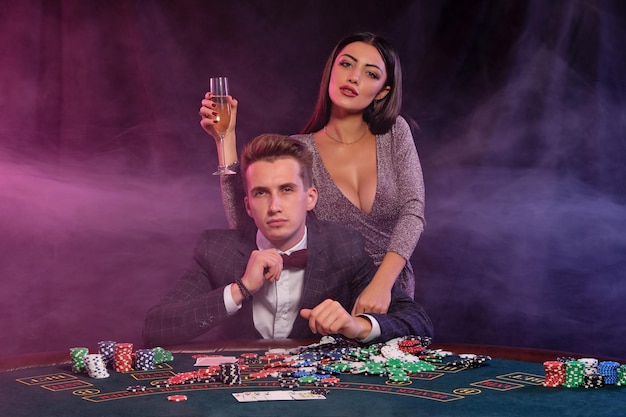 チップのスタックとお金のシャンパンカードを祝ってテーブルに座ってカジノでポーカーをプレイする男