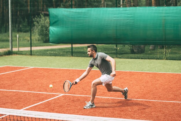 テニスをしている男。テニスコートでテニスをしているスポーツ服を着た自信のある青年