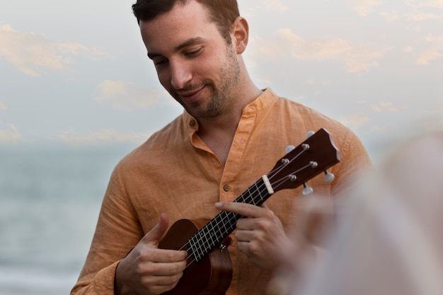 Foto uomo che suona l'ukulele in spiaggia