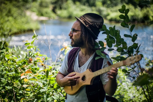 Foto uomo che suona l'ukulele in piedi contro le piante