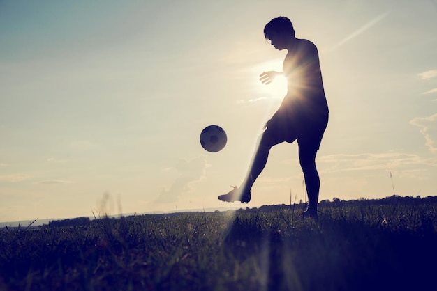 写真 夕暮れの空に向かって草の上でボールで遊ぶ男