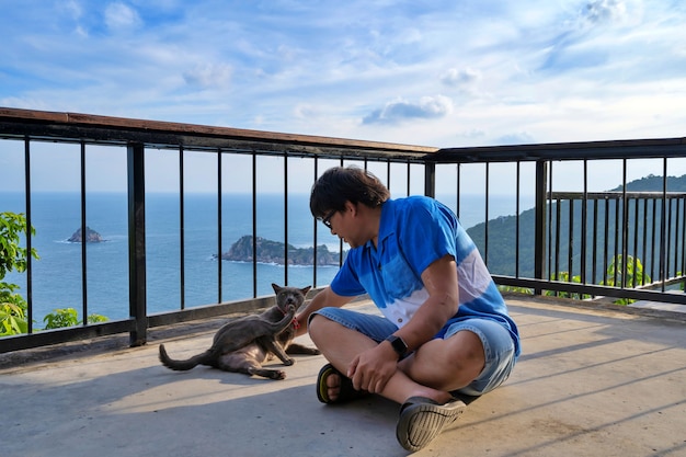 Man playing with cat on terrace floor with sea view