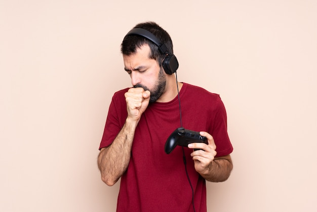 Man playing with a video game controller over isolated wall is suffering with cough and feeling bad