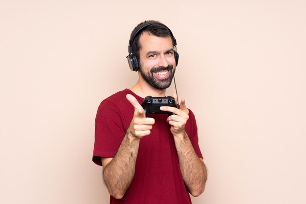 Man playing with a video game controller over isolated wall pointing to the front and smiling