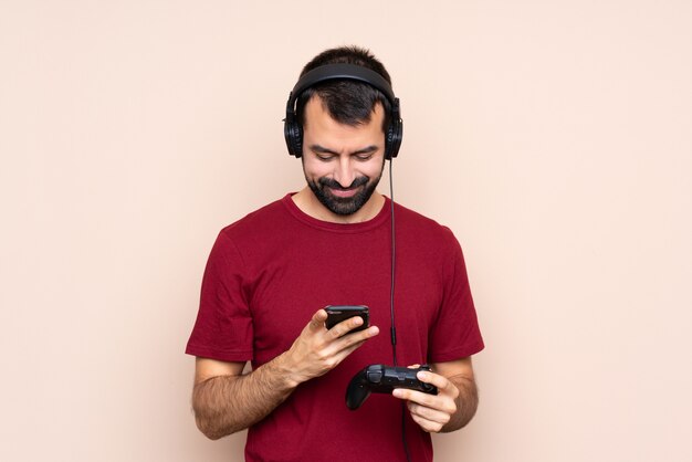 Man playing with a video game controller over isolated wall sending a message with the mobile