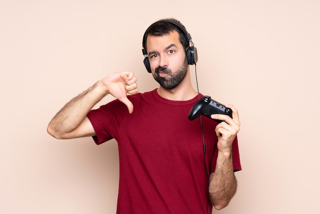 Man playing with a video game controller over isolated wall showing thumb down