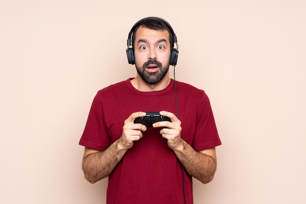 Man playing with a video game controller over isolated wall with surprise facial expression