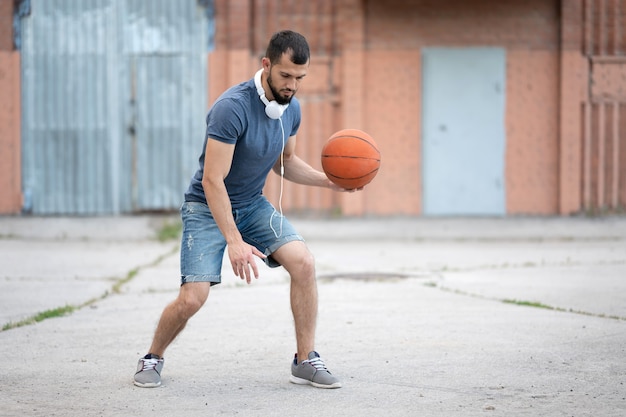Мужчина играет в баскетбол в уличном дворе днем