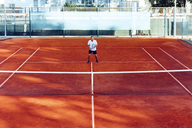 Man plays tennis on clay tennis field view from afar