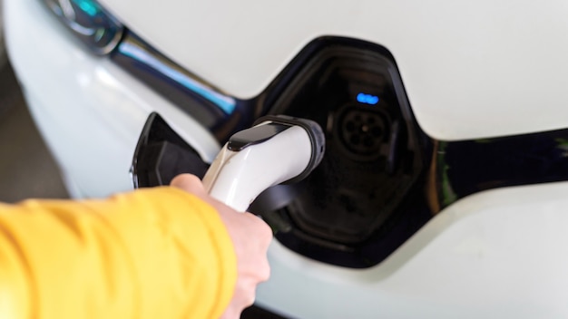 Man plugging in charger into an white electric car