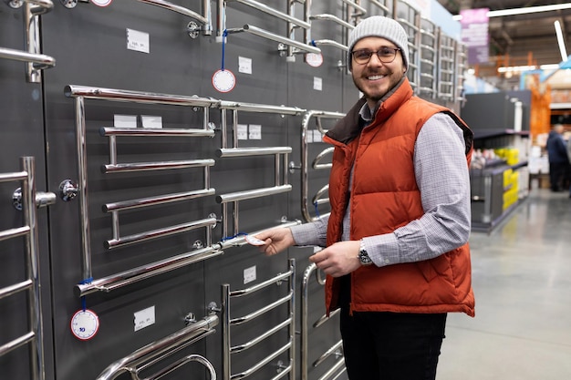 A man in a plumbing hypermarket chooses a chromeplated metal heated towel rail in the bathroom