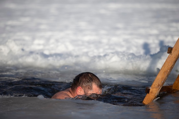 A man plunges into an ice-hole during the winter festival of the baptism of Jesus. A man swims in the ice-hole in winter. Walrus people.