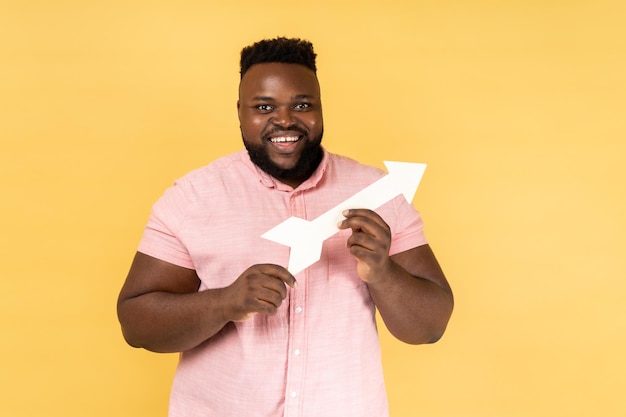 Man pointing direction with arrow aside looking at camera with positive expression