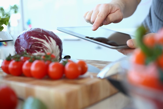 Фото Мужчина указывает пальцем на планшетный компьютер и на кухню со свежими овощами