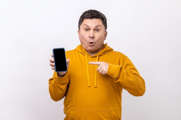 Man pointing finger at smartphone with empty screen looking at camera with shocked expression