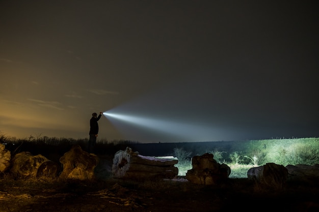 Man pointing flashlight to forest at night