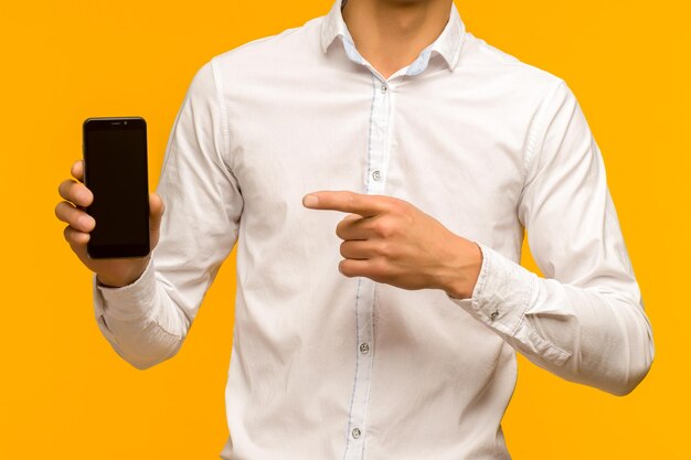 Мужчина указывает на мобильный телефон после получения хороших новостей на желтом фоне в студии