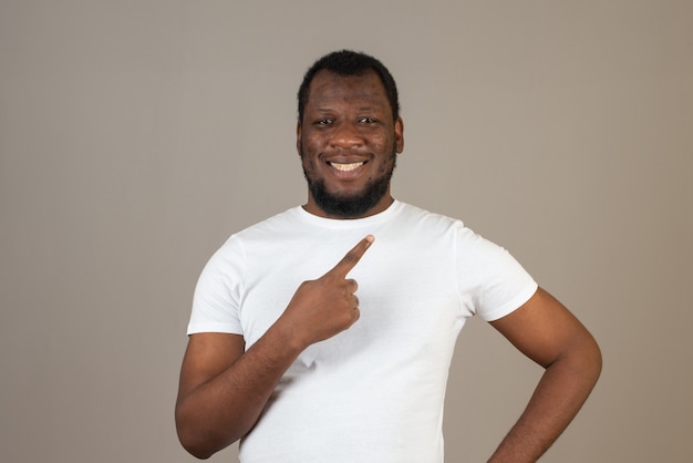 Man pointing up with his index finger ,standing in front of the grey wall