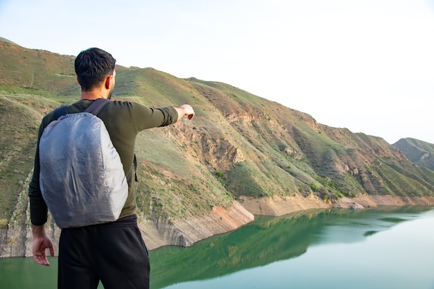 A man points to a point on a cliff by the lake