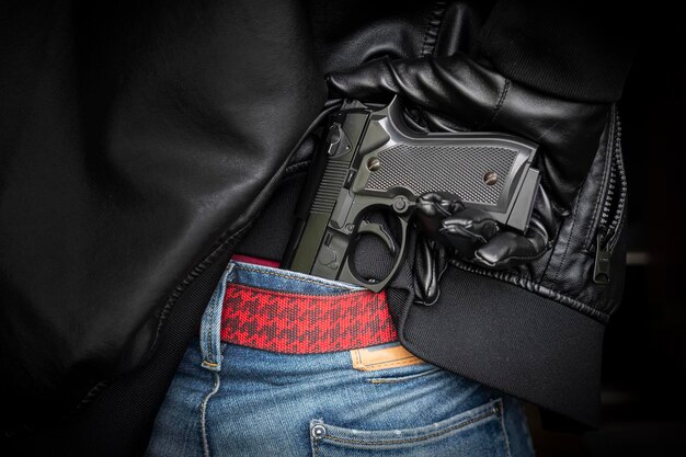 Мужчина-полицейский или грабитель-гангстер, скрывающий пистолет за спиной, стрелок вытаскивает огнестрельное оружие из-под черной кожаной куртки