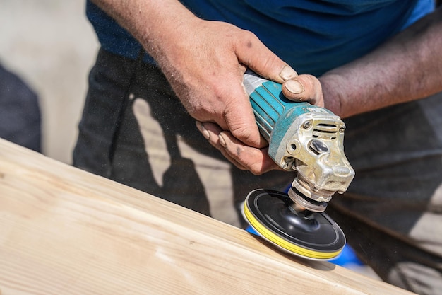 Photo man polishing wooden chest with old angle grinder during sunny day closeup detail to hands without gloves fine wood dust flying in air