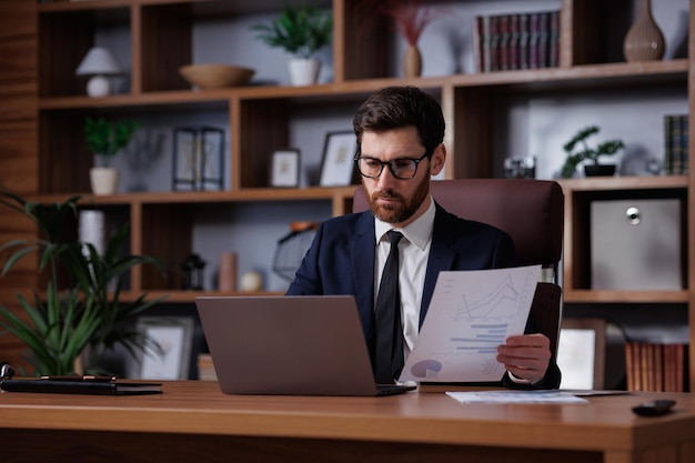 Man portrait in cinematographic light Handsome businessman is working in the office Work behind a laptop analysis of data and graphs