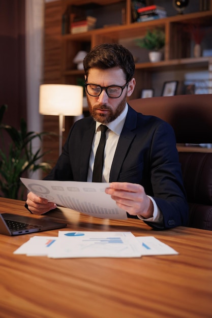 Man portrait in cinematographic light Handsome businessman is working in the office Work behind a laptop analysis of data and graphs