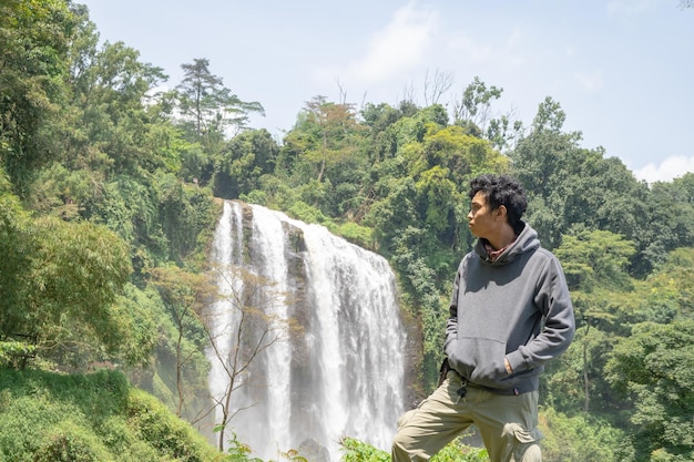 Man pose in front of the high water fall on the tropical forest