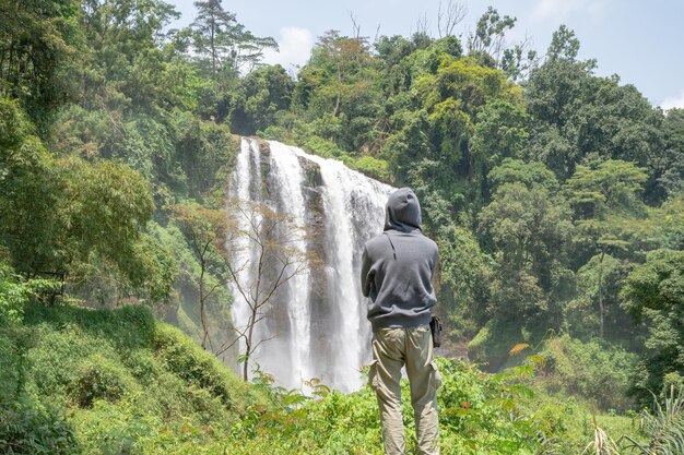 Man pose voor de hoge waterval op het tropische woud