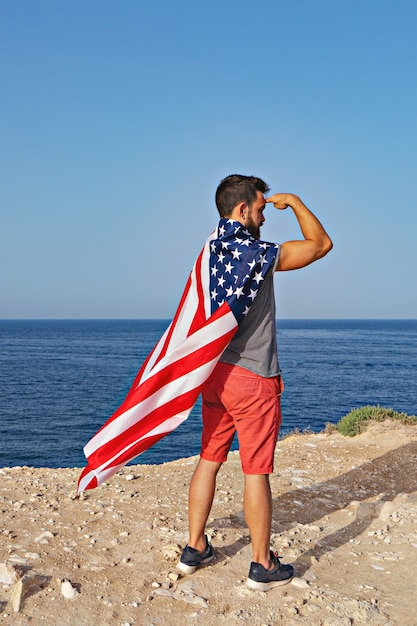 Man poseert in de vorm van held en Amerikaanse vlag als mantel buiten. Onafhankelijkheidsdag van de Verenigde Staten van Amerika. Concept van Amerikaanse patriottische mensen