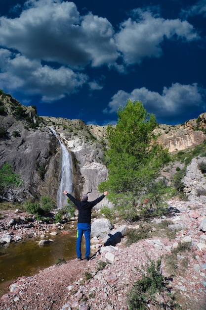 man poseren in rivier met waterval