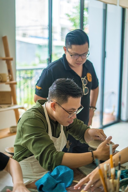 陶芸ワークショップのアートコンセプトで粘土から陶器の鍋を作る陶工の車輪に取り組んでいる男陶工フォーカス手若い男が粘土製品の一部を将来のセラミック製品に取り付ける陶器ワークショップ