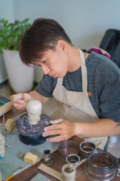 Man potter working on potters wheel making ceramic pot from\
clay in pottery workshop art concept focus hand young man attaching\
clay product part to future ceramic product pottery workshop