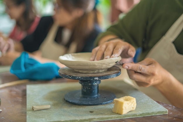 Man potter working on potters wheel making ceramic pot from\
clay in pottery workshop art concept focus hand young man attaching\
clay product part to future ceramic product pottery workshop