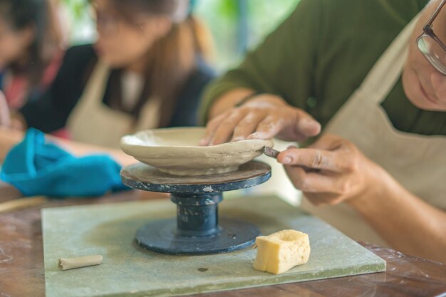 Man potter working on potters wheel making ceramic pot from clay in pottery workshop art concept Focus hand young man attaching clay product part to future ceramic product Pottery workshop