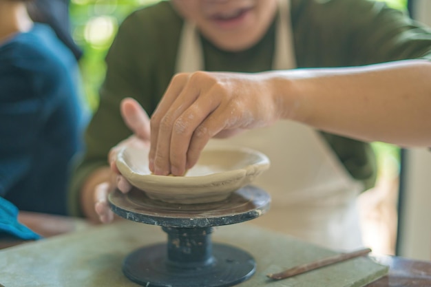 Man potter working on potters wheel making ceramic pot from clay in pottery workshop art concept Focus hand young man attaching clay product part to future ceramic product Pottery workshop