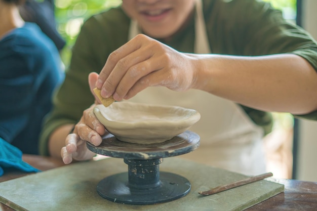 陶器ワークショップのアートコンセプトで粘土から陶器の鍋を作る陶工の車輪に取り組んでいる男陶工 フォーカス手若い男が粘土製品の一部を将来のセラミック製品に取り付ける 陶器ワークショップ