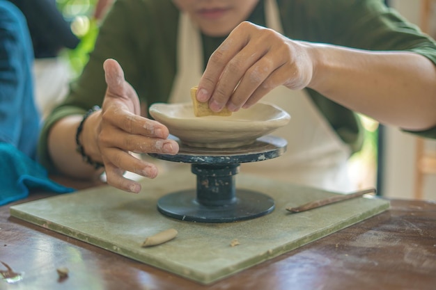 Man potter working on potters wheel making ceramic pot from\
clay in pottery workshop art concept focus hand young man attaching\
clay product part to future ceramic product pottery workshop