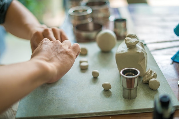 Man potter working on potters wheel making ceramic pot from clay in pottery workshop art concept Focus hand young man attaching clay product part to future ceramic product Pottery workshop