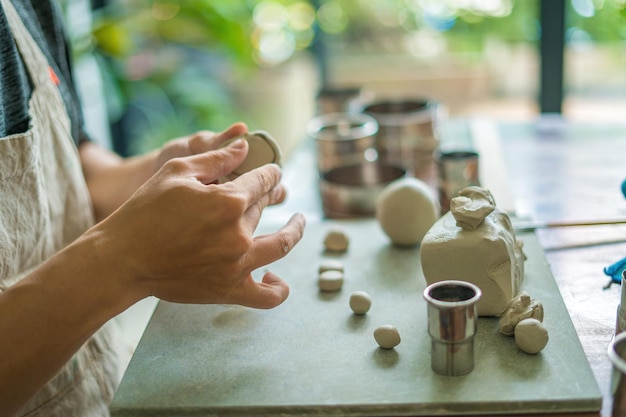 Man potter working on potters wheel making ceramic pot from\
clay in pottery workshop art concept focus hand young man attaching\
clay product part to future ceramic product pottery workshop