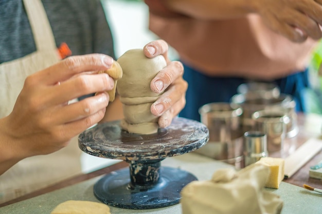 Man potter working on potters wheel making ceramic pot from\
clay in pottery workshop art concept focus hand young man attaching\
clay product part to future ceramic product pottery workshop