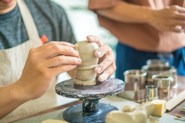 Man potter working on potters wheel making ceramic pot from\
clay in pottery workshop art concept focus hand young man attaching\
clay product part to future ceramic product pottery workshop