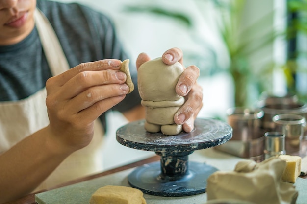 Man potter working on potters wheel making ceramic pot from\
clay in pottery workshop art concept focus hand young man attaching\
clay product part to future ceramic product pottery workshop