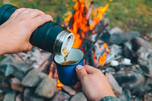 Man pour tea in metal cup camp fire on background