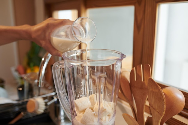 Man pouring nondiary milk in blender with cut bananas when making smoothie