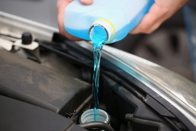 A man pours antifreeze from a canister into a car engine