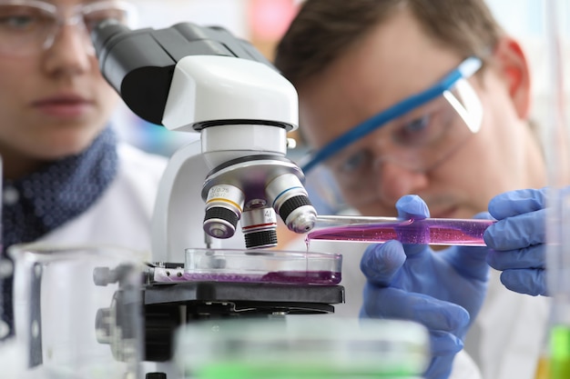 Man pours liquid into test tube under microscope